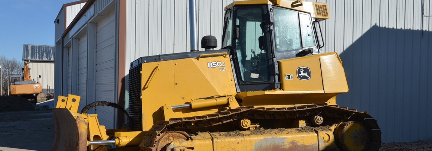 John Deere 850J LGP crawler dozer with blade parked beside a machine shed