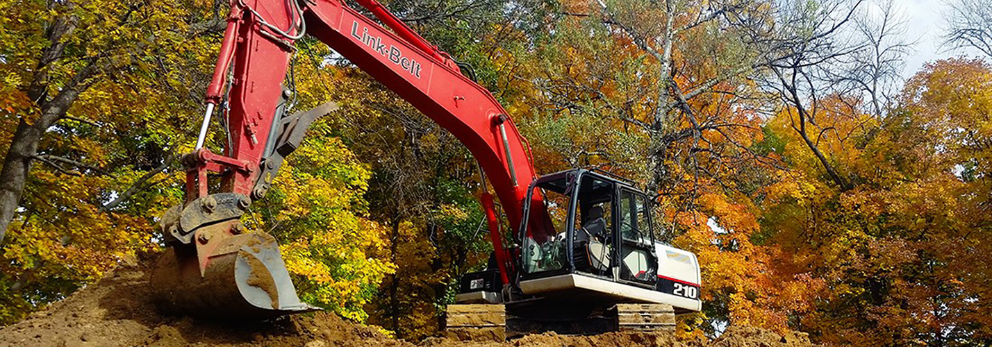 Link-Belt 210 excavator with a digging bucket working among autumn trees