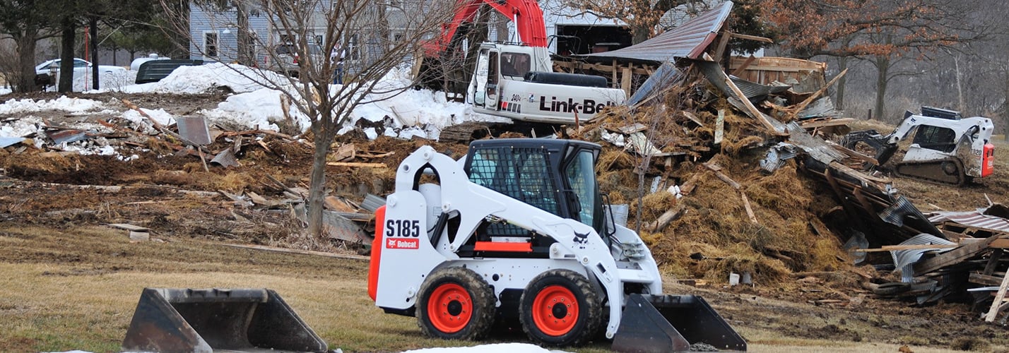 Bobcat S185 skid steer loader clearing storm debris beside a Link-Belt excavator